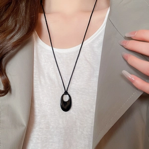 Vue détaillée d'un collier pendentif ovale creux porté avec un blazer gris et un t-shirt