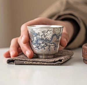 Primer plano de una taza de plata con motivos de dragón azul y olas sostenida a mano
