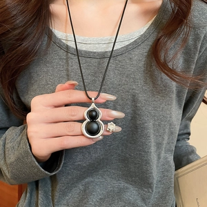 Collier à pendentif calebasse argenté avec pierres noires sur un pull en maille grise
