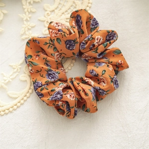 Close-up of orange floral fabric scrunchie with detailed rose pattern on lace background