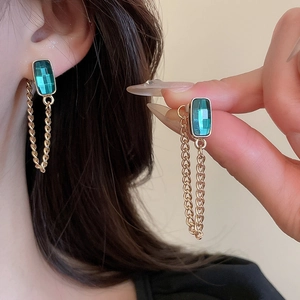 Close-up of emerald green rectangular gemstone earrings with elegant gold chain tassels