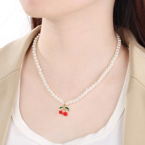 Close-up of elegant red cherry pendant on pearl necklace worn with a beige blazer