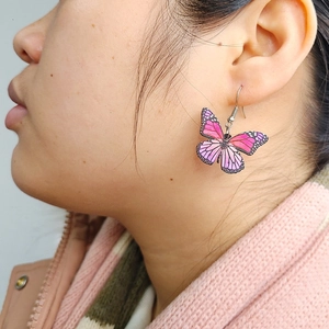 Detailed view of pink butterfly wing earrings on a model with gradient acrylic texture