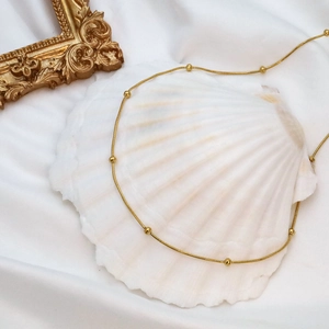 Macro view of 18k gold snake chain necklace with beads on elegant white silk fabric