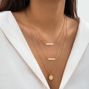 Detailed close-up of a three-layered gold necklace with pearls and a hammered round pendant