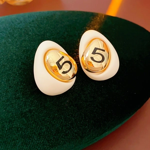 Macro view of gold-plated drop earrings with white enamel and black number 5 detail