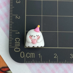 Mini resin ghost charm with birthday hat and heart, measured at 1.5cm on a grid mat
