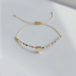 Detail eines verstellbaren Perlenarmbands mit goldenem T-Anhänger im Boho-Stil