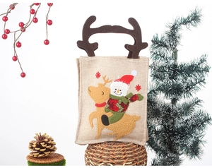 Close-up of burlap Christmas gift bag with reindeer antlers and festive snowman appliqué
