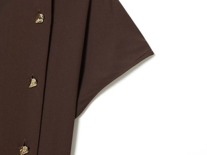 Détail du tissu marron café d'une robe avec un bouton doré irrégulier de style moderne