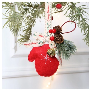 Detail of red wool felt glove ornament with snow embroidery and gold bell hanging on pine