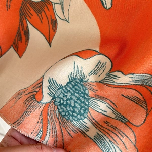 Close-up of magnolia cashmere-feel scarf fabric showing detailed orange floral weave texture