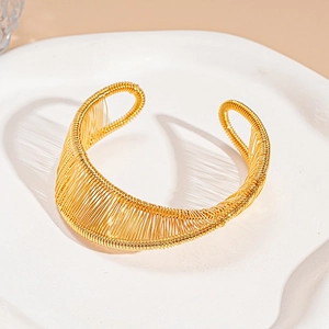 Detail of gold spiral wire wrapped open cuff bracelet on white decorative tray