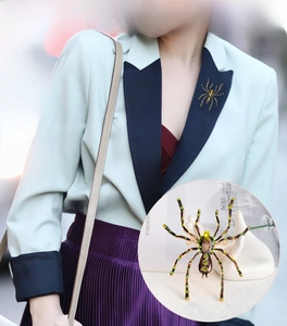 Detailed view of an oversized spider brooch featuring emerald green crystals and striped legs