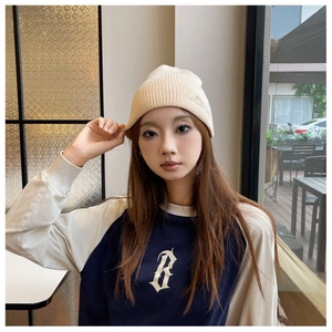 Detail of off-white ribbed knit beanie with small embroidery and contrast raglan sleeve tee