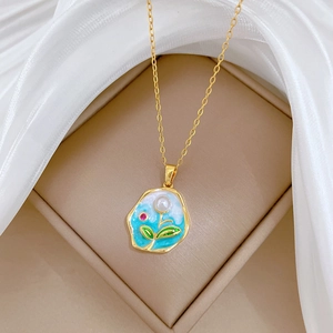Detailed shot of gold necklace with blue enamel floral pendant and pearl in jewelry box