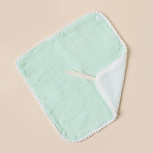 Detail of baby muslin bib with white pom-pom trim and snap buttons in mint green