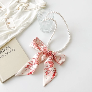 Detail of a pearl necklace with a vintage red and white pattern fabric scarf bow
