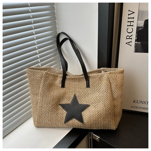 Detail of woven straw tote bag with black leather star patch and long shoulder straps