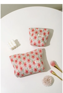 Detail of floral knit cosmetic bags with textured fabric and woven label on a white table