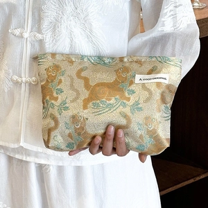 Detail of fabric handbag featuring gold and green tiger pattern held by a model