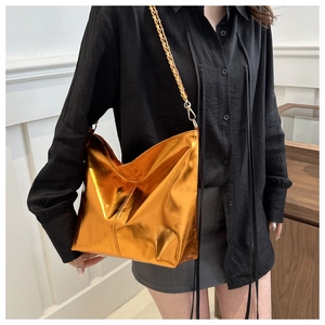 Detail of orange metallic shoulder bag with gold chain strap on a model outfit