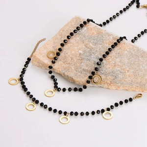 Elegant black beaded necklace with gold circular pendants on natural stone display