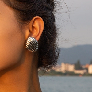 Gros plan d'une boucle d'oreille argentée côtelée portée sous un coucher de soleil