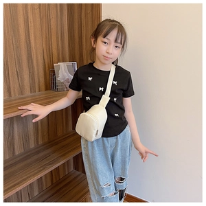 Toddler in black tee styling a cream white crossbody chest bag on a wooden staircase