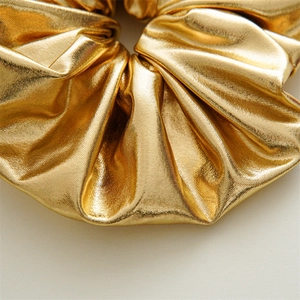 Detail of golden metallic scrunchie showing rich pleats and shiny textured fabric surface
