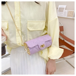 Detail view of lavender quilted cylindrical bag with golden chain on model attire