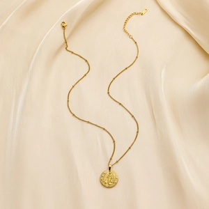 Detail of gold coin zodiac relief necklace on beige silk fabric with lobster clasp