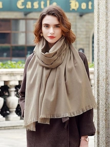 Detail of khaki cashmere scarf with soft fringes worn by a model in an outdoor setting