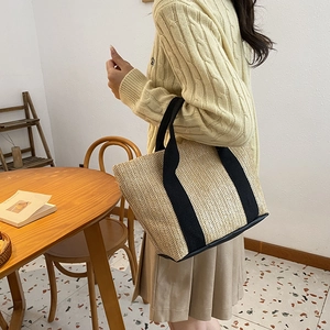 Minimalist straw tote bag with black canvas straps shown in a natural lifestyle setting