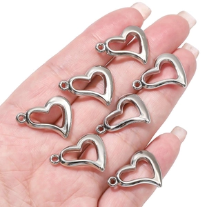 Close-up of seven silver heart bow pendants held in palm showing scale and luster