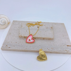 Macro view of gold-plated heart pendant with pink enamel detail on beige stone plates