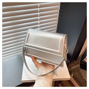 Detailed view of a silver metallic crossbody bag held by a model in a trendy studio