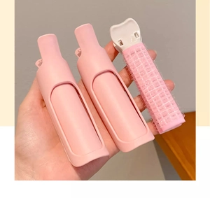 Close-up of hand holding pink and white hair root volume clips and hair rollers set