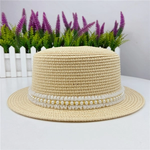 Détail de la dentelle blanche avec perles et fil doré sur un chapeau canotier en paille