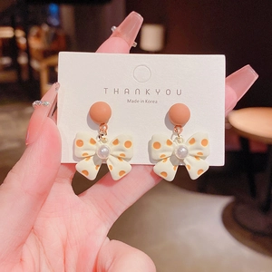Detail of sweet bow earring with orange polka dots and elegant faux pearl charms