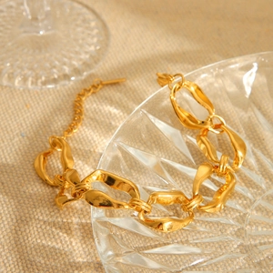 Detail of 18K gold irregular chain link bracelet on decorative glass and beige fabric
