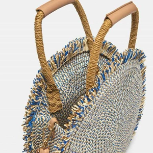 Round woven straw beach bag in beige and blue with tassel edge and twin rope handles