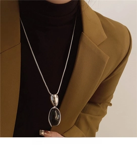 Detail of a vintage oval black resin pendant necklace on a silver chain and wool sweater