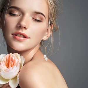 Model wearing gold hoop earrings with layered white pearls and delicate metal chain