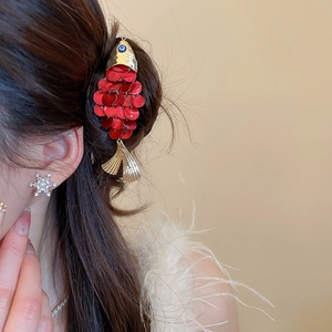 Detail of red shell fish hair clip with gold scales worn by model on beige background