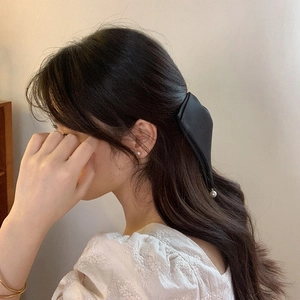 Detail of a black satin bow hair clip with a pearl pendant on brunette wavy hair