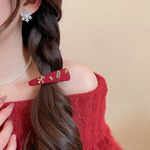 Close-up of a festive red wool felt hair clip with golden horse and coin charms on a model