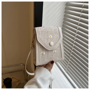 Detail of beige straw phone bag with daisy embroidery and flap closure held by hand