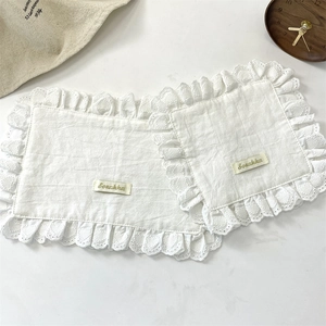 Detail of two white cotton linen coasters with delicate lace edges and Szakka label