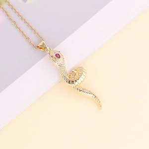 Macro detail of a 18K gold snake pendant with sparkling zircon inlay and red gemstone eyes